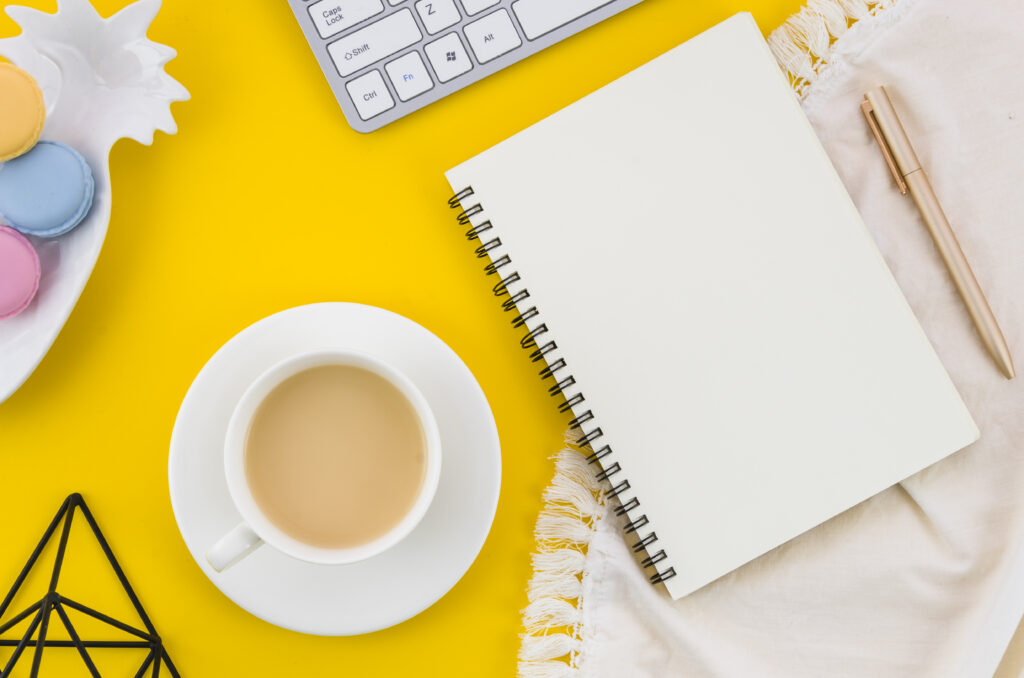 taza de te macarrones libreta de espiral pluma sobre mantel contra fondo amarillo